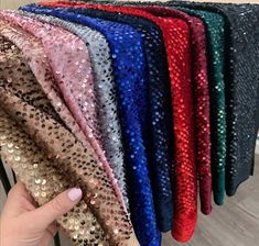 a person holding up some sequins in front of a rack of different colors