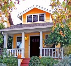 a small yellow house with white trim and red steps leading up to the front door