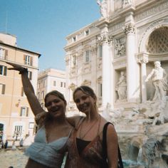 two women standing next to each other in front of a building with statues on it