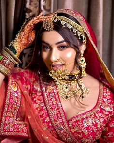 a woman in a red and gold bridal outfit with jewelry on her head, posing for the camera