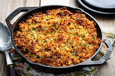 a skillet filled with macaroni and cheese on top of a wooden table