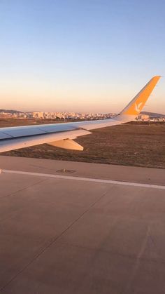 the wing of an airplane as it flies over some grass and buildings in the distance