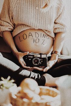 a pregnant woman holding a camera with the words loading 40 written on her stomach