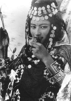 an old photo of a woman wearing a headdress and holding something in her hand