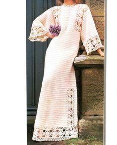 a woman in a white crochet dress and hat standing next to a door