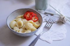 a bowl filled with pasta next to a fork and knife on top of a table