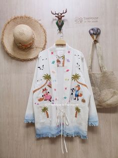 a white jacket with cartoon characters on it next to a straw hat and other items