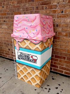 a large ice cream cone with sprinkles on it sitting in front of a brick wall