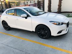 a white mazda car parked in front of a parking lot with palm trees behind it