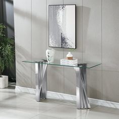 a glass table with metal legs in a room next to a potted plant and pictures on the wall