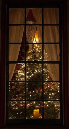 a lit christmas tree is seen through a window