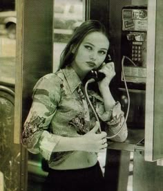 a woman is talking on the phone while standing next to an old fashioned payphone