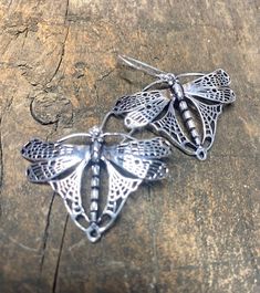 two silver butterfly brooches sitting on top of a piece of wooden table next to each other