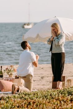 a woman holding an umbrella standing next to a man on the beach