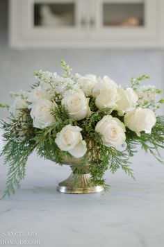 a vase filled with white flowers sitting on top of a marble countertop covered in greenery