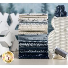 a stack of different colored fabrics next to a white vase and snowflakes