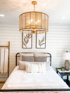 a bed with white sheets and pillows under a light hanging from the ceiling above it