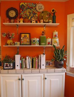 an orange room with white cupboards and shelves filled with books, pictures, and other decorative items