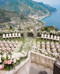 an outdoor ceremony set up with white chairs and flowers on the ground, overlooking water