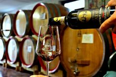 a person pouring wine into a glass in front of barrels