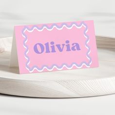 a pink place card sitting on top of a white plate with a blue border around it