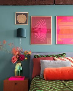 a bedroom with blue walls and pictures on the wall above the bed, along with a colorful vase filled with flowers