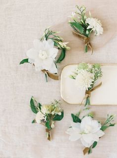 white flowers and greenery are arranged on a table cloth, along with an empty tray