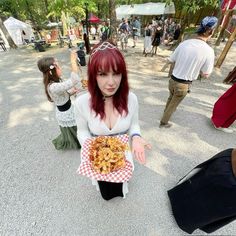 a woman with red hair holding a plate of food in front of other people at an outdoor event