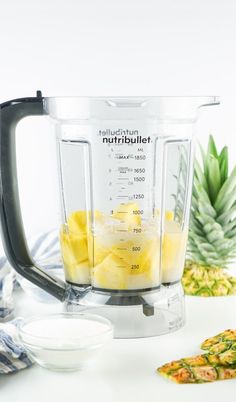 a blender filled with pineapples next to other ingredients on a white surface