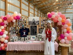 a woman is standing in front of a table with balloons and photos on the wall