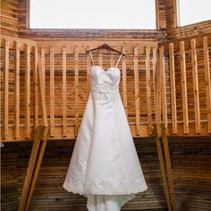 a wedding dress hanging on a rack in front of a wooden wall with windows and wood slats