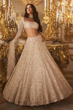 a woman standing in front of a mirror wearing a gold colored lehenga and crop top