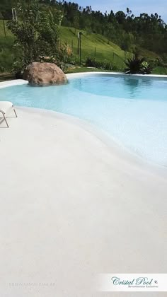 an empty lawn chair sitting in front of a pool with a rock on the side