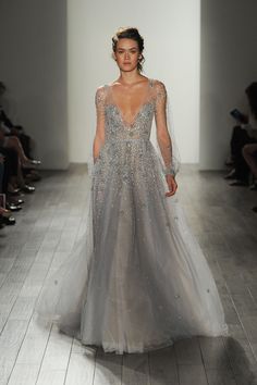 a woman in a long dress walking down the runway wearing a white and silver gown