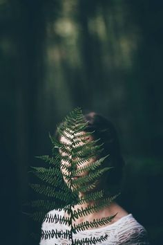 a woman is standing in the woods with a fern leaf on her head and she's back turned to the camera