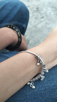 a person sitting on the ground with their arm wrapped around her wrist and wearing a silver bracelet