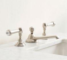 two chrome faucets sitting on top of a white counter