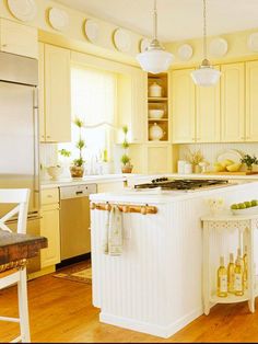 a kitchen with yellow cabinets and white counter tops, an island that has wine bottles on it