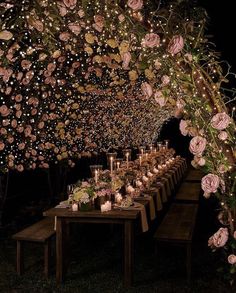 a long table with candles and flowers on it is lit up in the dark at night