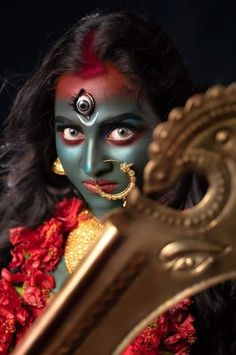 a woman with painted face and body holding a large metal object in front of her face