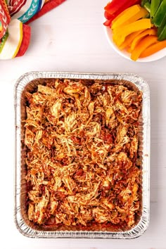 a casserole dish with meat and vegetables in the background on a white table