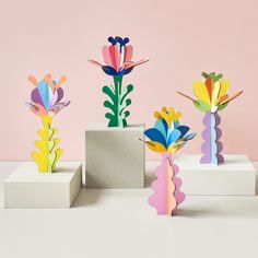 three vases with colorful paper flowers in them on a table next to a pink wall