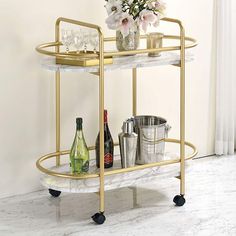 a gold bar cart with drinks and glasses on the top is sitting in front of a window