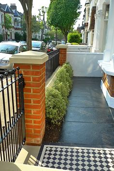 a black and white checkerboard sidewalk next to a brick wall with an iron gate