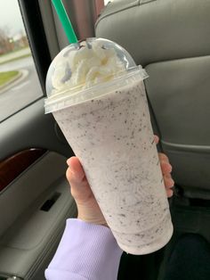 a person holding up a drink in the back seat of a car with a green straw