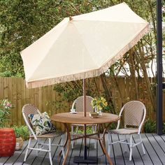 an umbrella is on top of a wooden table with chairs and a potted plant