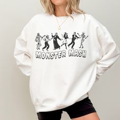 Rock this hauntingly cute Monster Mash Halloween crewneck sweathisrt! Featuring classic Halloween villains in a retro cartoon style, this sweatshirt is perfect for fans of spooky season, the Monster Mash, or anyone who wants a festive look with a touch of nostalgia. Stay spooky and grab yours today!  -50% Cotton 50% Polyester -Loose fit -Sewn in label -Runs true to size (size up for oversized fit) -Inclusive sizing: S-3XL All items are made-to-order: - We do not accept returns, size changes or cancellations. Please read size charts for these items. - Returns and exchanges are only available for damaged or wrong items. Retro Long Sleeve Halloween Tops, Horror Crew Neck Sweatshirt For Fall, Fall Horror Crew Neck Sweatshirt, Horror Style Crew Neck Sweatshirt For Fall, White Graphic Print Sweatshirt For Halloween, Funny Halloween Graphic Print Sweatshirt, Horror Themed Halloween Sweatshirt With Graphic Print, Halloween Character Print Sweatshirt For Streetwear, Halloween Band Merch Long Sleeve Sweatshirt