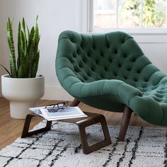 a green chair sitting on top of a white rug next to a potted plant