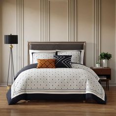 a bed with black and white comforter in a bedroom next to a lamp on a wooden floor