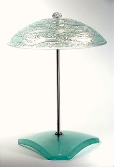 an umbrella shaped glass table lamp on a stand with a white back ground and light behind it